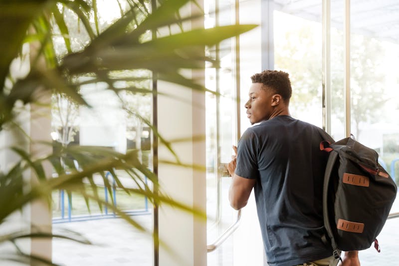 A student with a backpack stepping out of a campus building, ready to study abroad