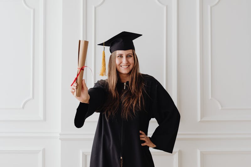 A smiling graduate in cap and gown holding a diploma